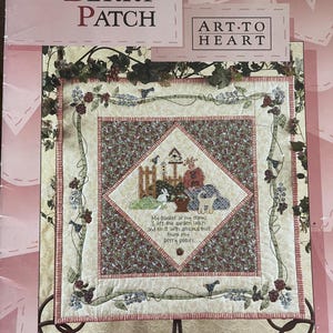 May include: A decorative quilt with the text "IN MY BERRY PATCH" and "ART-TO HEART". The quilt features a central diamond design with a garden scene, surrounded by floral and bird motifs. The text "My basket at my elbow..." is also visible.