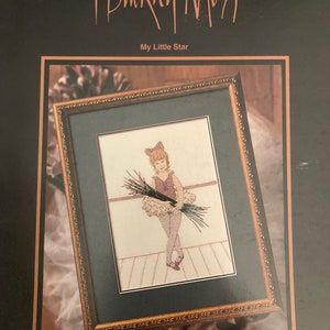 May include: A cross-stitch pattern featuring a young girl in a pink tutu holding a bouquet of flowers. The pattern is framed in a gold frame and is titled "My Little Star" by June Grigg Designs Inc. The pattern is from Buckley Moss Leaflet 133, Limited Edition.