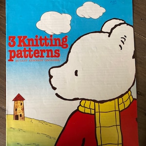 Può includere: Un libretto di modelli di maglia vintage con Rupert l'orso, un orso bianco che indossa un maglione rosso e una sciarpa gialla. La copertina ha uno sfondo di cielo blu con nuvole bianche e il testo "3 modelli di maglia di Gary Kennedy (Intarsia)".