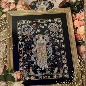 Könnte beinhalten: Gerahmtes Kreuzstich-Kunstwerk mit dem Titel "Flora" mit einem goldenen Rahmen. Das Design zeigt eine zentrale Figur in einem fließenden Kleid, umgeben von floralen und blattartigen Motiven auf dunklem blauem Hintergrund. Rahmenmaße: 38 cm x 51 cm.
