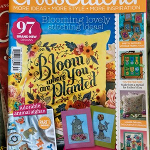 May include: A stack of magazines with the top one titled "Cross Stitcher." The cover features a yellow pillow with floral embroidery and the phrase "Bloom where you are planted." Other articles include "Adorable animal afghan" and "Pawfect Pups."