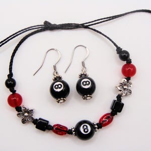 May include: A black beaded bracelet and matching earrings set. The bracelet and earrings feature black and red beads, silver-tone flower accents, and black 8-ball beads. The earrings have silver-tone hooks.