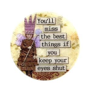 May include: A round, colorful, vintage-style image with a fairy-like figure wearing a crown and holding a wand. The text reads "You'll miss the best things if you keep your eyes shut."