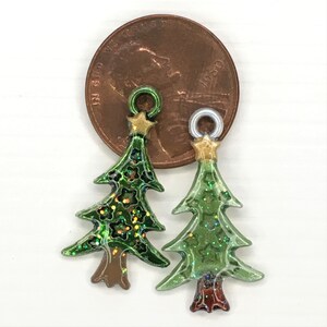 May include: Two green glitter Christmas tree ornaments with gold star toppers and brown bases. The ornaments are about the size of a US penny.