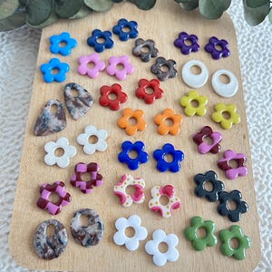 May include: A collection of colorful flower-shaped beads and pendants in various colors, including blue, pink, red, orange, yellow, and green. The beads are arranged on a wooden surface, ideal for crafting or jewelry making.