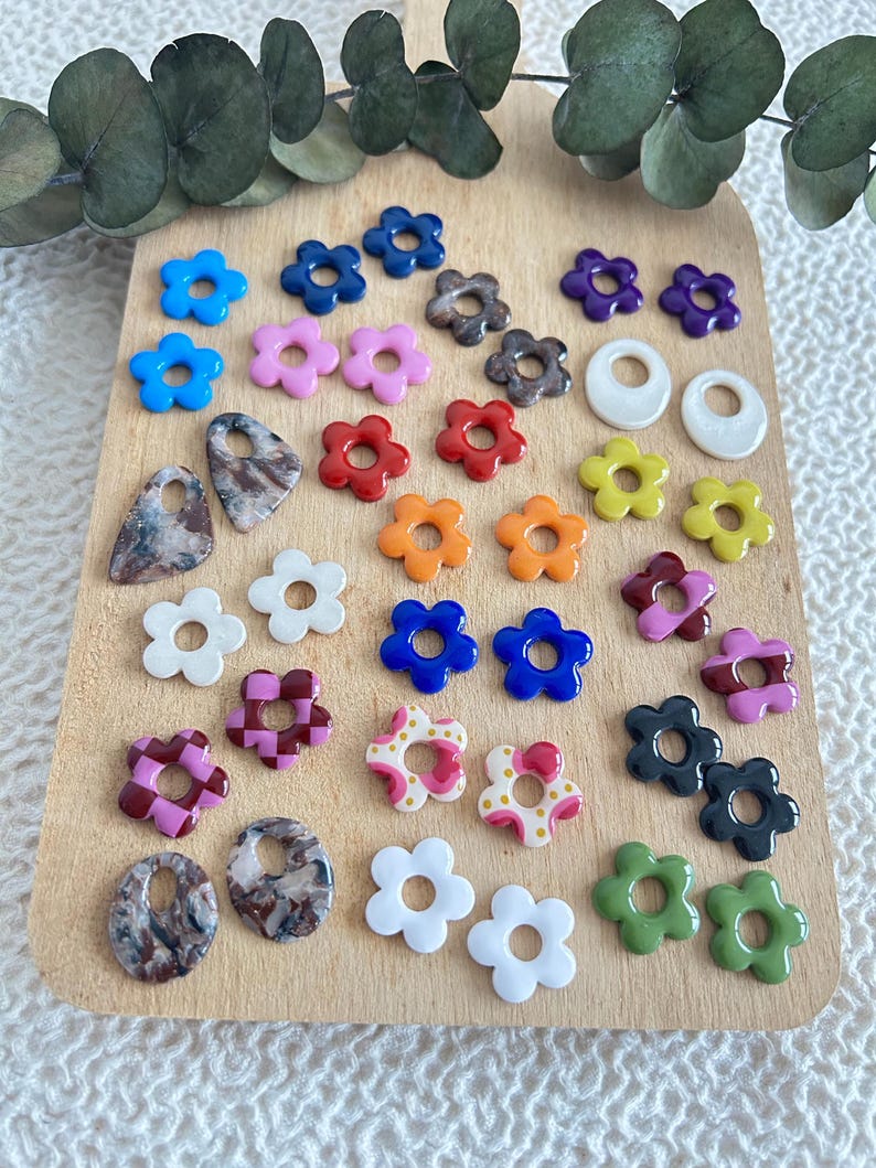 May include: A collection of colorful flower-shaped beads and pendants in various colors, including blue, pink, red, orange, yellow, and green. The beads are arranged on a wooden surface, ideal for crafting or jewelry making.