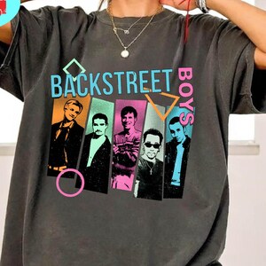 May include: Dark gray t-shirt featuring the text "BACKSTREET BOYS" above a graphic of the band members. The shirt has a vintage look and is made of a soft material. The shirt also has the text "PEPPER COMFORT COLORS".