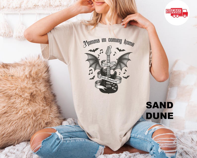 Puede incluir: Camiseta color arena con un dise&ntilde;o gr&aacute;fico en blanco y negro de una guitarra con alas de murci&eacute;lago, notas musicales y el texto "Momma I'm coming home" y "Ozzy Osbourne 1948-2023".