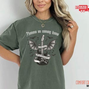 Puede incluir: Camiseta Comfort Colors verde musgo con un gr&aacute;fico de guitarra alada, el texto "Momma I'm coming home" y "Ozzy Osbourne 1948-2023". La camiseta tiene un corte relajado y est&aacute; hecha de material suave.