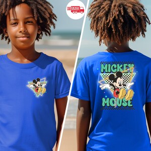 May include: Royal blue t-shirt featuring Mickey Mouse. The front has a small graphic of Mickey in a triangle, while the back displays "Mickey Mouse" in a retro font with a checkered background. The shirt is short-sleeved.