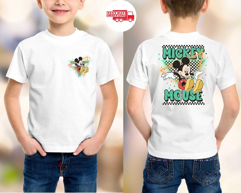 May include: White t-shirt featuring Mickey Mouse. The front has a small graphic of Mickey, while the back displays a larger design with the words "Mickey Mouse" in green and black, with a checkered pattern.