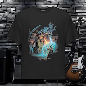 Może przedstawiać: Czarny t-shirt z krótkim rękawem z nadrukiem graficznym przedstawiającym smoka siedzącego na kamiennym zamku, ziejącego ogniem w stronę czarodzieja rzucającego zaklęcie świecącej niebieskiej tarczy ochronnej. Koszulka posiada małą prostokątną metkę.