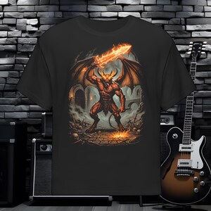 Puede incluir: Una camiseta negra con un estampado gráfico de un demonio musculoso y alado con cuernos, que sostiene una espada en llamas y un látigo. El demonio se encuentra en un entorno de mazmorra de piedra oscura con calaveras y armas esparcidas.