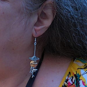 Op de afbeelding: Zilveren oorhangers met een gouden bol en een zilveren ring, en twee zilveren dolfijnen die eronder hangen.