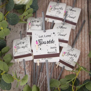 May include: Wedding sparklers with white labels that say "Let Love Sparkle" with the couple's names and wedding date. The labels also have a small pink matchstick on them.