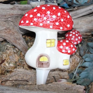 May include: A ceramic mushroom house with a red and white spotted cap, a white body, and two yellow windows. The house has a small brown door with a yellow window.