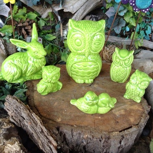 May include: A collection of green ceramic figurines, including a rabbit, owls, and a pair of birds, arranged on a tree stump. The figurines are all in a bright green color and have a textured finish.