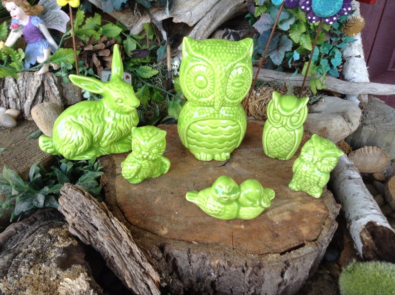 May include: A collection of green ceramic figurines, including a rabbit, owls, and a pair of birds, arranged on a tree stump. The figurines are all in a bright green color and have a textured finish.