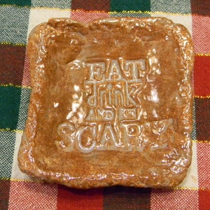 May include: A brown ceramic dish with a raised, white inscription that reads "Eat, Drink and Be Scary".