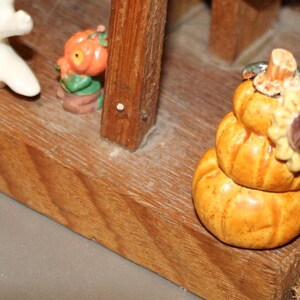 May include: A wooden tiered stand with a ghost, a pumpkin, and a stack of three pumpkins with a sunflower on top. The stand is painted brown and has a rustic look.