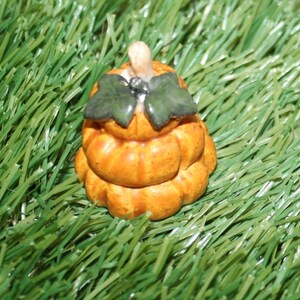 May include: A small ceramic pumpkin figurine with a stacked design, featuring a green leaf stem and a light brown stem. The pumpkin is a light orange color and has a textured surface.