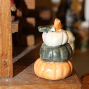 May include: A stack of three ceramic pumpkins, the top one is white, the middle one is green, and the bottom one is orange.