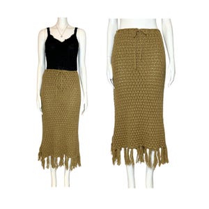 May include: A tan crochet skirt with a drawstring waist and fringe detail. The skirt is displayed on a mannequin, paired with a black top. The skirt's texture and design are clearly visible, showcasing its handmade quality.