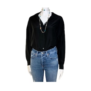 May include: A black long-sleeve button-down shirt paired with blue denim jeans. A multi-strand necklace with colorful beads and pearls is worn with the shirt. The outfit is displayed on a mannequin.
