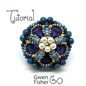 Puede incluir: Primer plano de un colgante de flor de cuentas con un esquema de color azul, morado y dorado. El colgante está hecho con cuentas de semillas y presenta un diseño floral central con un centro de perla.