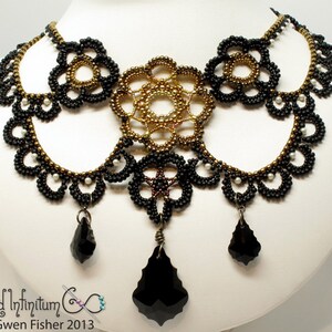 May include: A black and gold beaded necklace with a large, intricate centerpiece and three dangling black crystal drops. The necklace is on a white background.