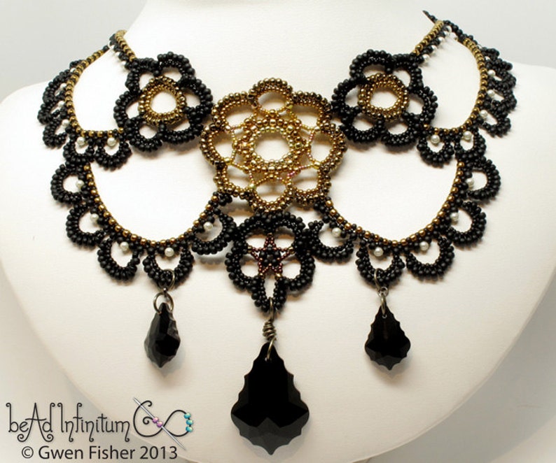 May include: A black and gold beaded necklace with a large, intricate centerpiece and three dangling black crystal drops. The necklace is on a white background.