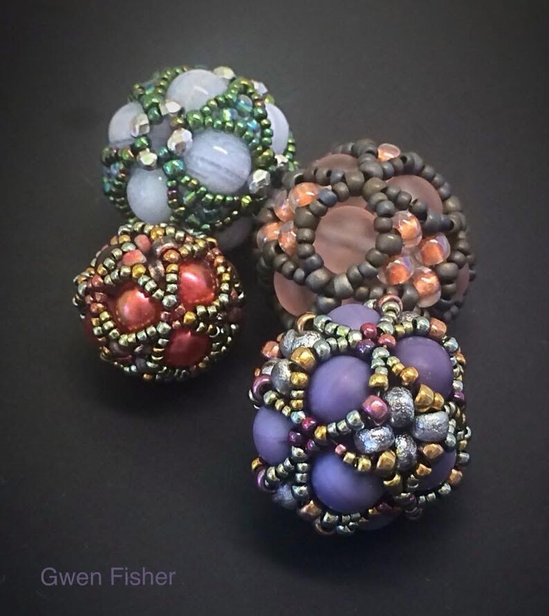 Peut inclure: Quatre sph&egrave;res perl&eacute;es de diff&eacute;rentes couleurs. L'une est rouge et or, une autre est violette et argent&eacute;e, une troisi&egrave;me est verte et bleue, et la derni&egrave;re est marron et orange. Les sph&egrave;res sont finement perl&eacute;es avec une vari&eacute;t&eacute; de tailles et de couleurs de perles. Le nom de l'artiste, Gwen Fisher, est en bas.