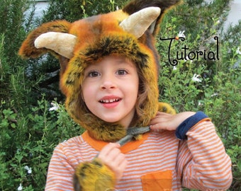 May include: A child wearing a striped shirt and a furry orange, brown and black animal hat with horns. The hat has a long tail that the child is holding. The text "Tutorial" is visible in the background.