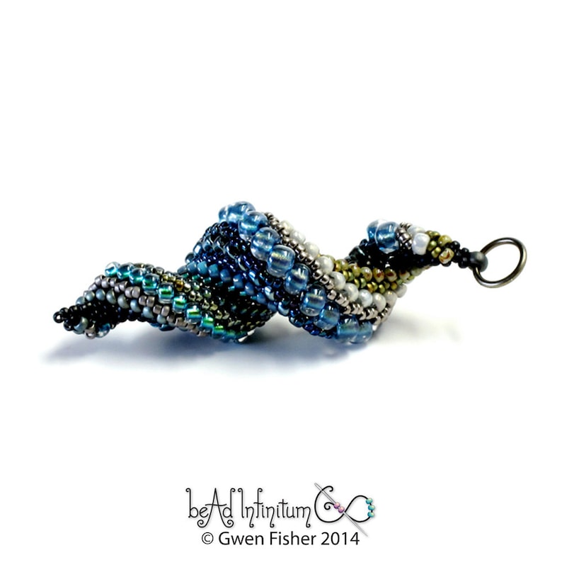 May include: A beaded spiral pendant in shades of blue, green, silver, and white. The pendant is made with small seed beads and has a silver loop at the top for attaching to a chain or cord.