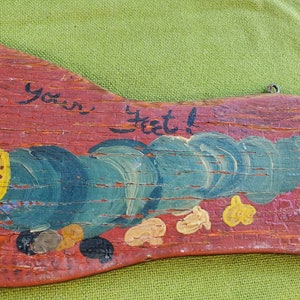 May include: A hand-painted wooden sign with a red background and the words "Wipe your feet!" in black script. The sign features a whimsical design with blue and yellow painted details, and a metal loop for hanging.