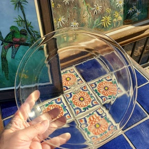 May include: A clear glass pie plate with a slightly rippled edge. The plate is held in a hand and reflects a colorful tiled surface.