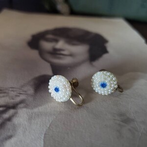 May include: A pair of vintage clip-on earrings with a white pearl design and a blue center. The earrings are made of metal and have a gold tone finish.