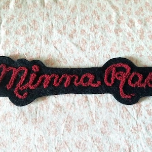 May include: A black felt patch with the words "Mimma Rae" embroidered in red thread.
