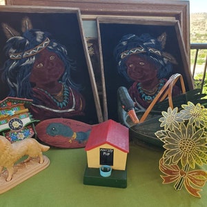 May include: A selection of vintage decorative items, including framed portraits of Native American children, a cuckoo clock, a wooden fish, a dog figurine, a bird feeder, and a floral decoration. The items are displayed on a green surface.