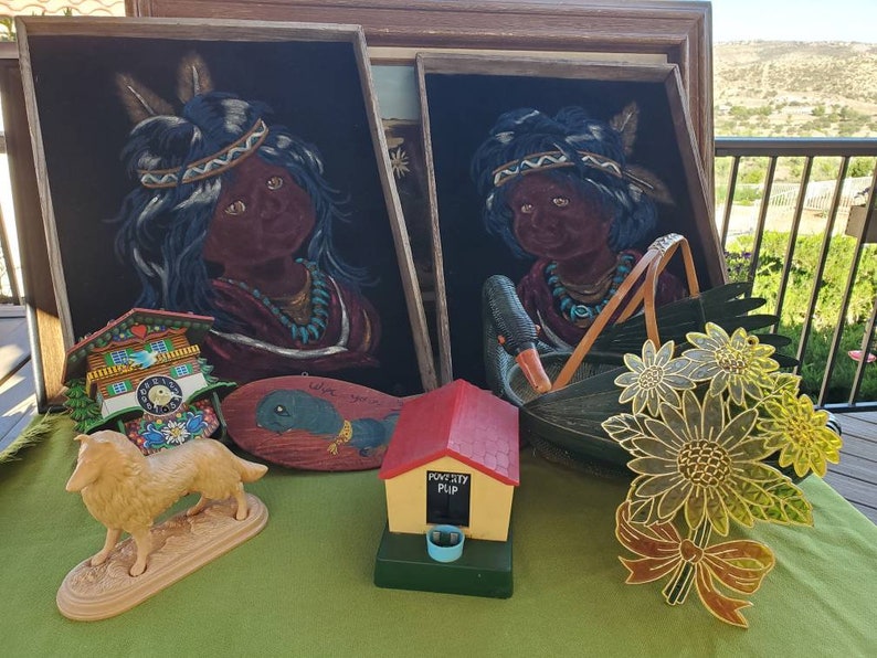 May include: A selection of vintage decorative items, including framed portraits of Native American children, a cuckoo clock, a wooden fish, a dog figurine, a bird feeder, and a floral decoration. The items are displayed on a green surface.