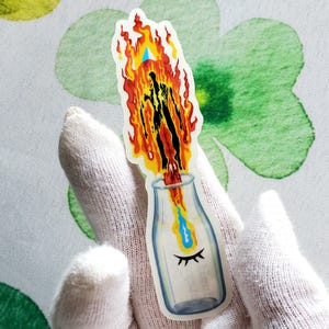 Puede incluir: Una pegatina de una botella de leche de vidrio con una persona envuelta en llamas que sale de la parte superior. Las llamas son de color naranja, amarillo y rojo. La persona es negra y la botella es transparente con un ojo azul dibujado en la parte delantera.