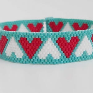 May include: A turquoise beaded bracelet with a repeating pattern of white and red hearts.
