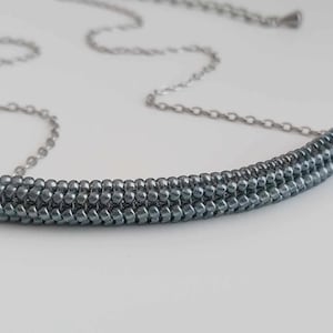 May include: A silver chain necklace with a grey beaded bar pendant. The beads are arranged in a graduated pattern, creating a subtle ombre effect.