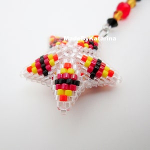 May include: A beaded star charm with red, yellow, and black stripes. The star is made of clear beads and is attached to a silver chain.