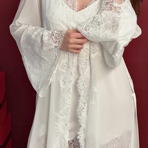 Pode incluir: Conjunto de lingerie branco com um roup&atilde;o transparente com acabamento em renda. O roup&atilde;o tem mangas compridas com punhos largos de renda e um acabamento em renda a condizer na frente e na bainha. O conjunto inclui uma camisola e cal&ccedil;&otilde;es, tamb&eacute;m com detalhes em renda.