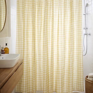 Può includere: Una tenda da doccia con un motivo a quadretti vichy giallo chiaro e bianco. La tenda è appesa a un'asta in metallo argentato tramite una serie di anelli argentati, creando pieghe verticali che si estendono dalla parte superiore a quella inferiore.