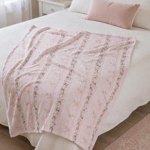 May include: A soft throw blanket featuring a repeating pattern of vertical pink stripes and delicate floral vines with green leaves and small pink flowers. The blanket measures 50 inches by 60 inches and is draped over a white bedspread.
