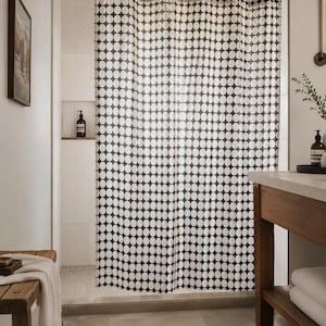 Puede incluir: Un baño moderno con una cortina de ducha de lunares blancos y negros. La cortina cuelga de una barra negra. El baño tiene un tocador de madera, una alfombra tejida y un banco de madera.