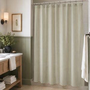 May include: A shower curtain featuring a vertical striped pattern in alternating shades of sage green and white. The fabric hangs from a silver metal rod with matching circular rings, creating uniform folds across the length of the curtain.