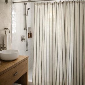 May include: A shower curtain featuring a vertical striped pattern in dark gray and off-white. The curtain hangs from a metal rod with rings, covering a shower area with white subway tile walls, a handheld showerhead, and a rainfall showerhead.
